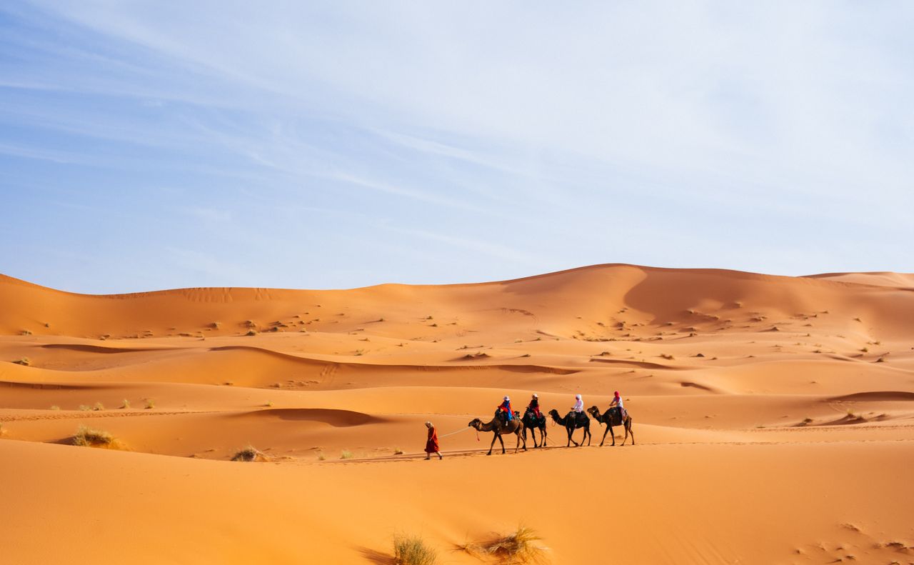 Tourists riding camels across the dunes of Merzouga, Morocco, a popular Sahara destination.