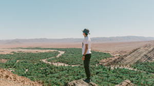 A man stands on a rock, gazing over a lush oasis in Tata, Morocco.