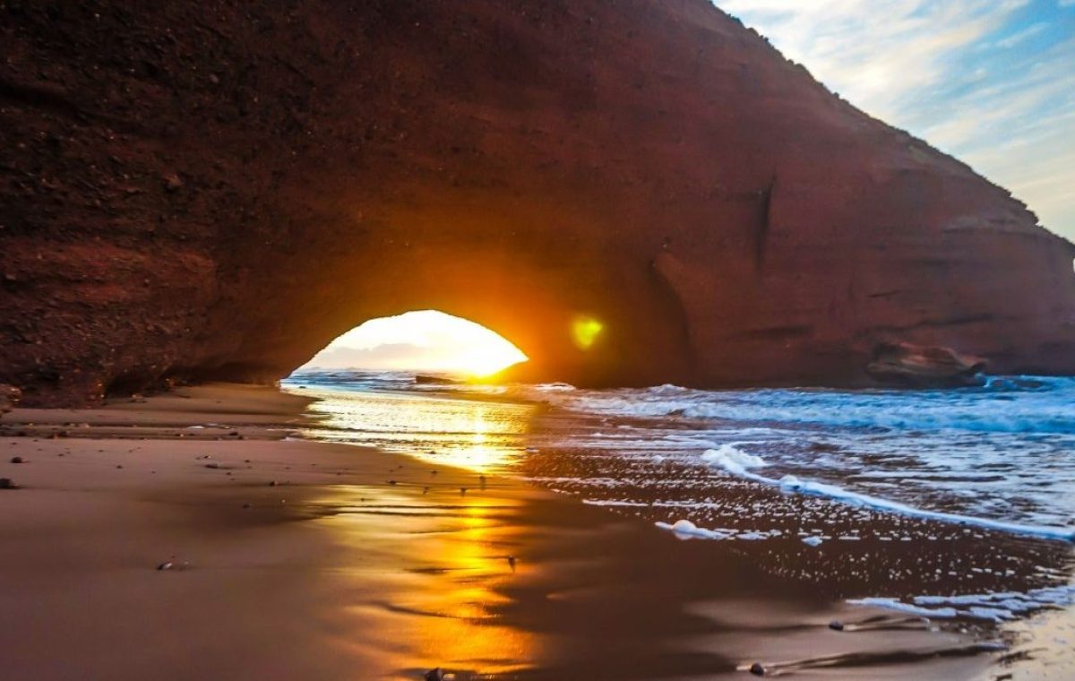 Sunset through the red rock arch on Legzira beach, on a Morocco tour from Casablanca