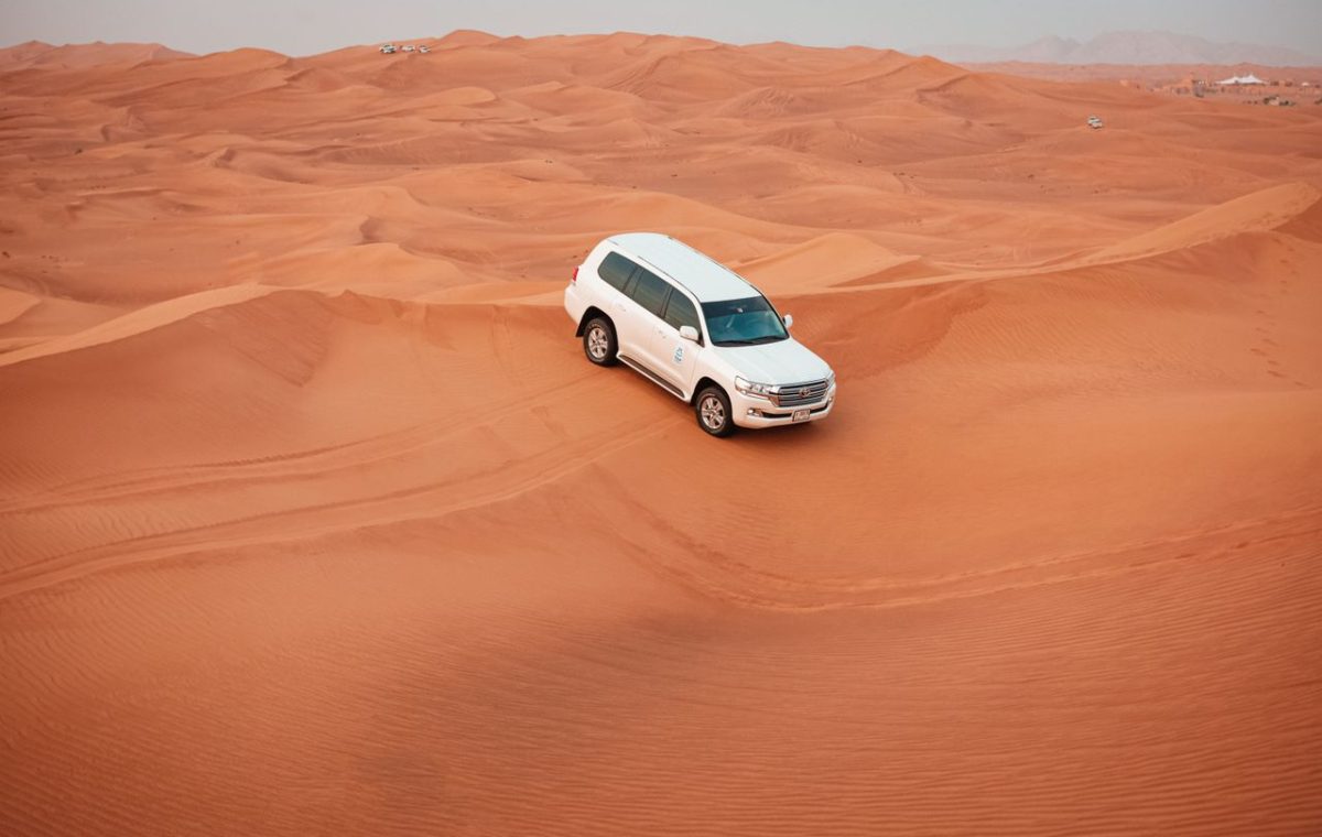 White 4x4 driving across sand dunes